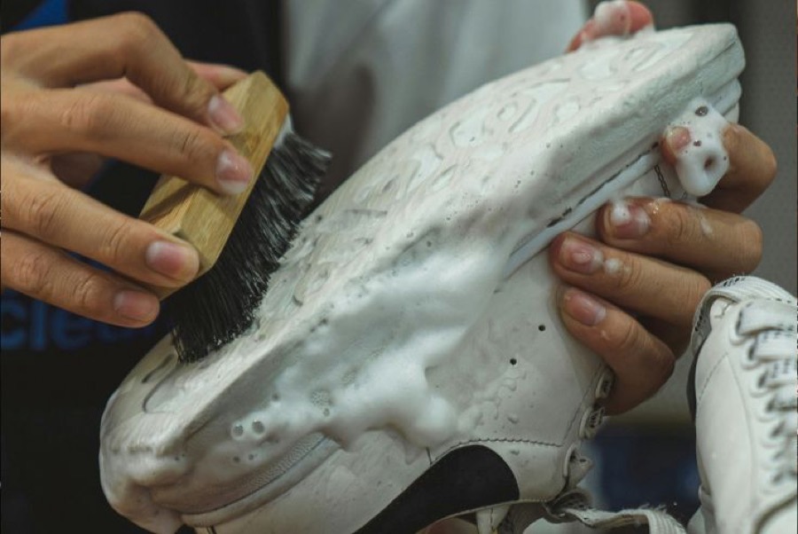A white sneaker being deep-cleaned with foam and a brush